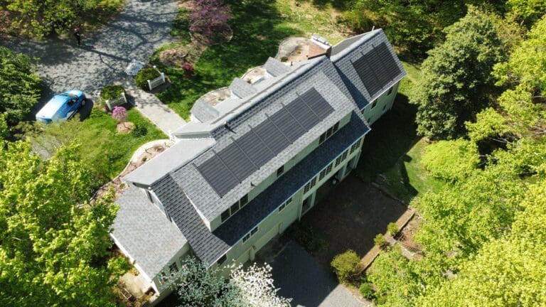 a house with gaf timberline solar shingles as roof in the spring and a driveway surrounded by trees